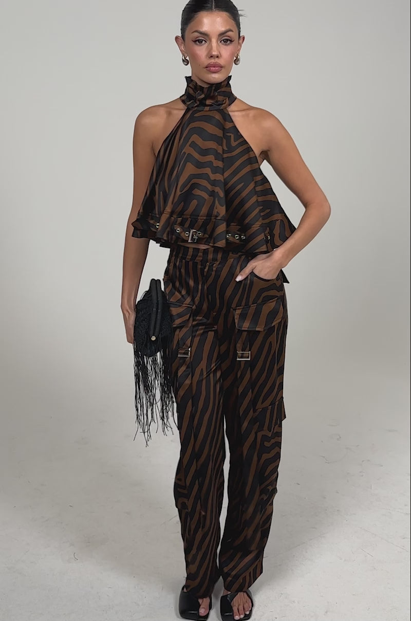 Video of woman modeling the INTO THE WILD ZEBRA TROUSER with a matching halter top, accessorized with a black fringed clutch and black sandals against a plain light background.