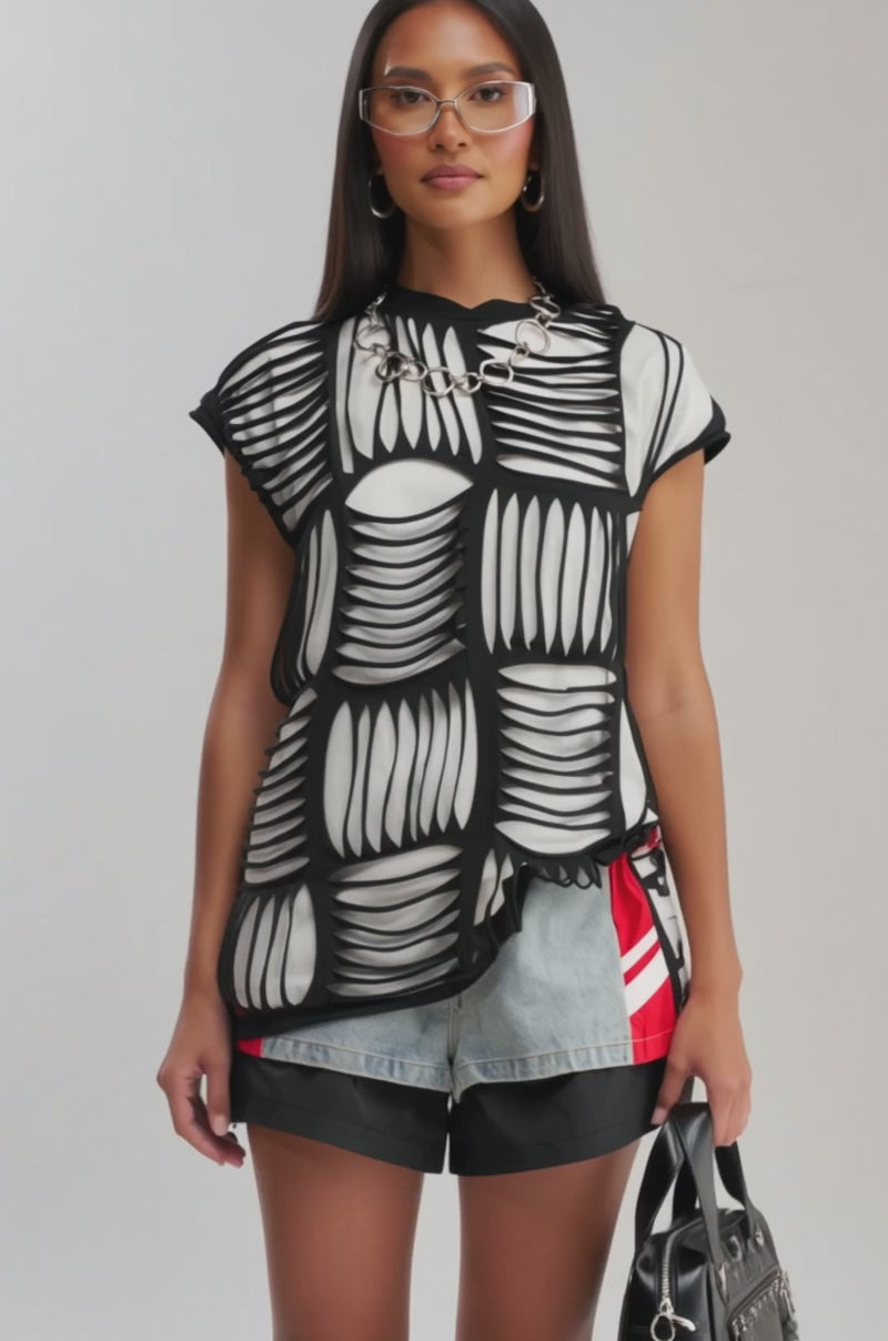 Video of woman modeling the STRESSED OUT DISTRESSED TEE with a striking black-and-white geometric pattern over black shorts, standing against a plain light background.