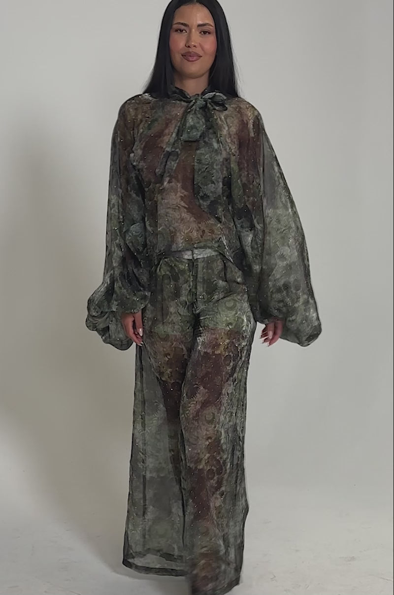 Video of woman modeling the MYSTIQUE FLORAL CHIFFON BLOUSE, featuring sheer balloon sleeves, earth-toned floral patterns, and a large neck bow. 