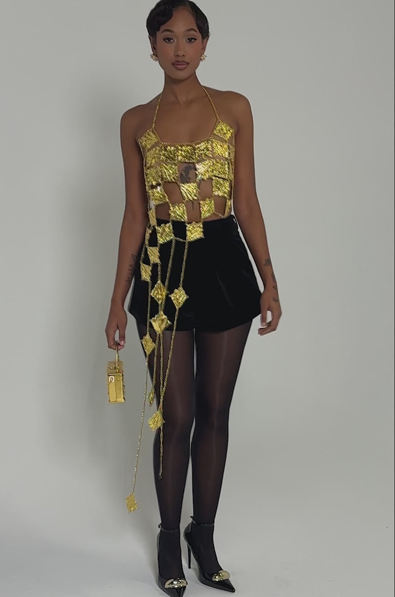 Video of woman modeling the SHOW ME WHAT YOU GOT METAL CHAIN TOP, styled with black shorts, sheer tights, black heels, and a gold handbag—creating a bold statement look against a plain light background.