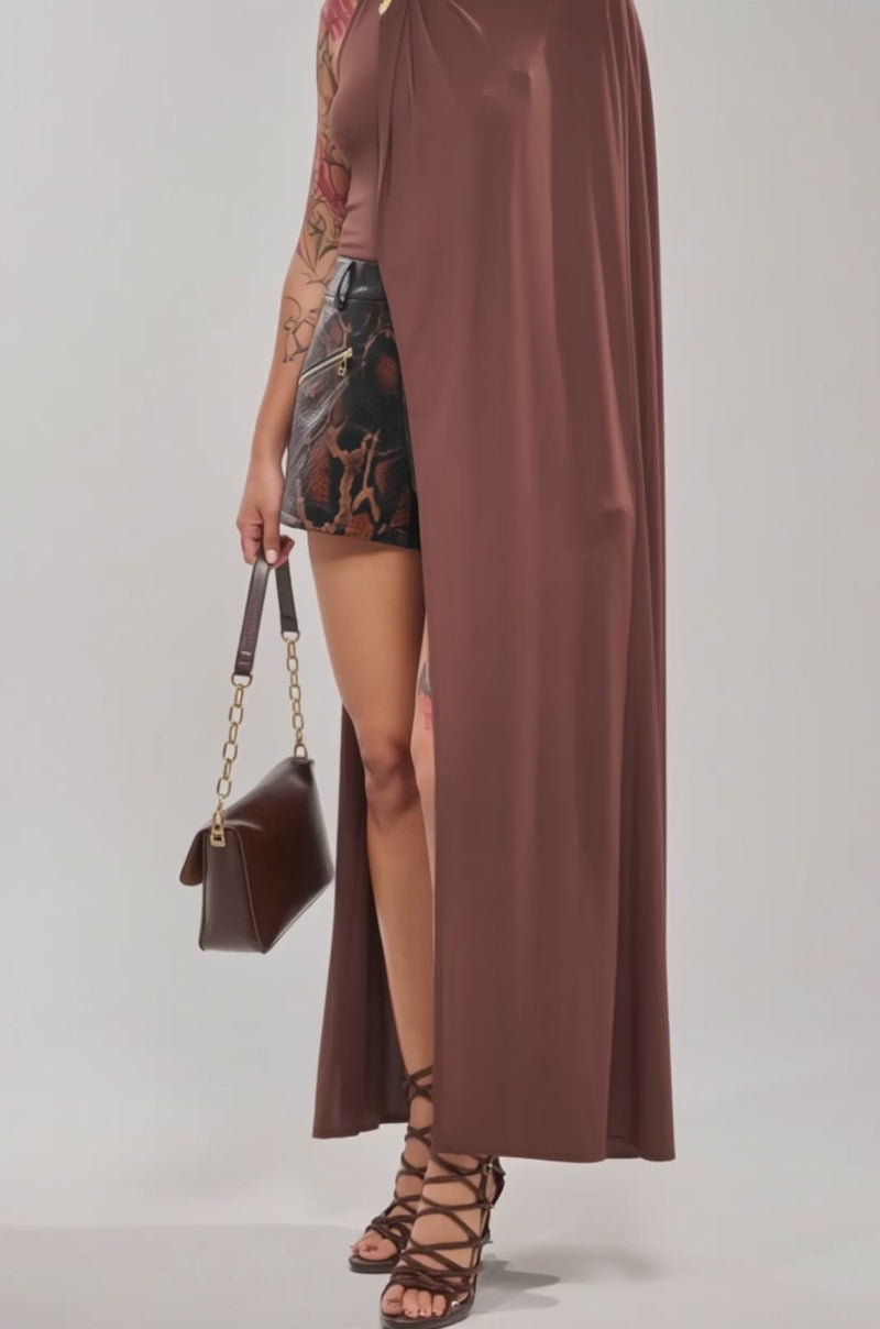 A video of a woman in the NOT YOURS CAPE BODYSUIT, styled with patterned shorts, lace-up high heels, and a brown handbag with a gold buckle.