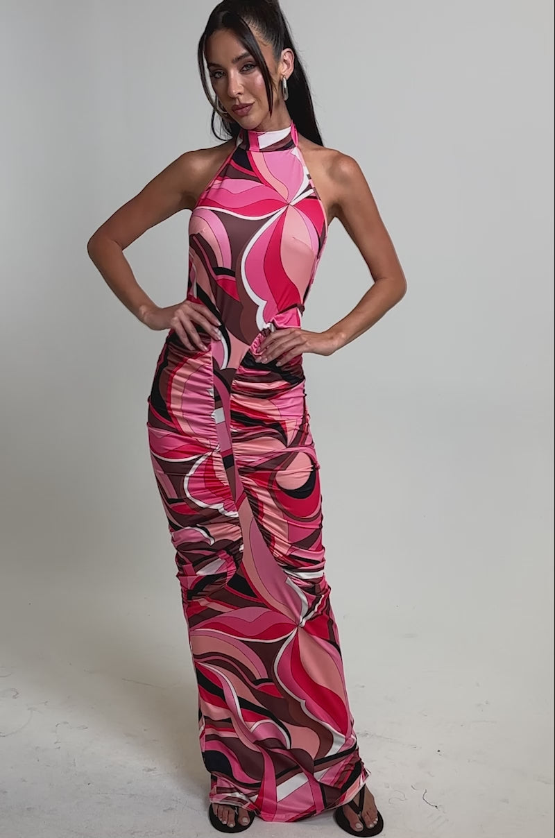 A video of a woman wearing the PERFECTLY EXTRA HIGH NECK PRINTED MAXI DRESS, a sleeveless, floor-length dress featuring a vibrant pink, red, and brown abstract swirl print.
