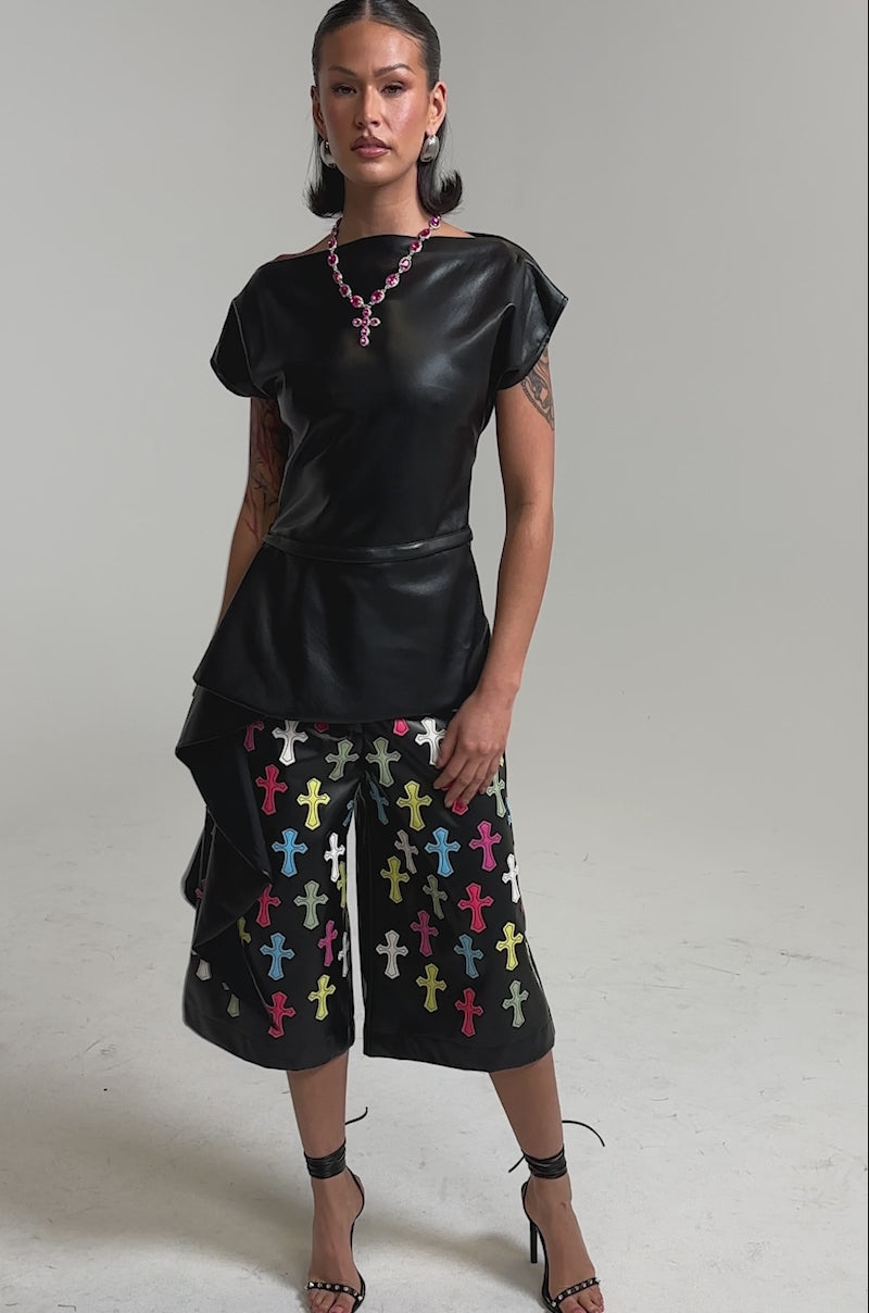 A video of a woman wearing the ALEXA FAUX LEATHER BLOUSE and culottes with colorful cross patterns. 