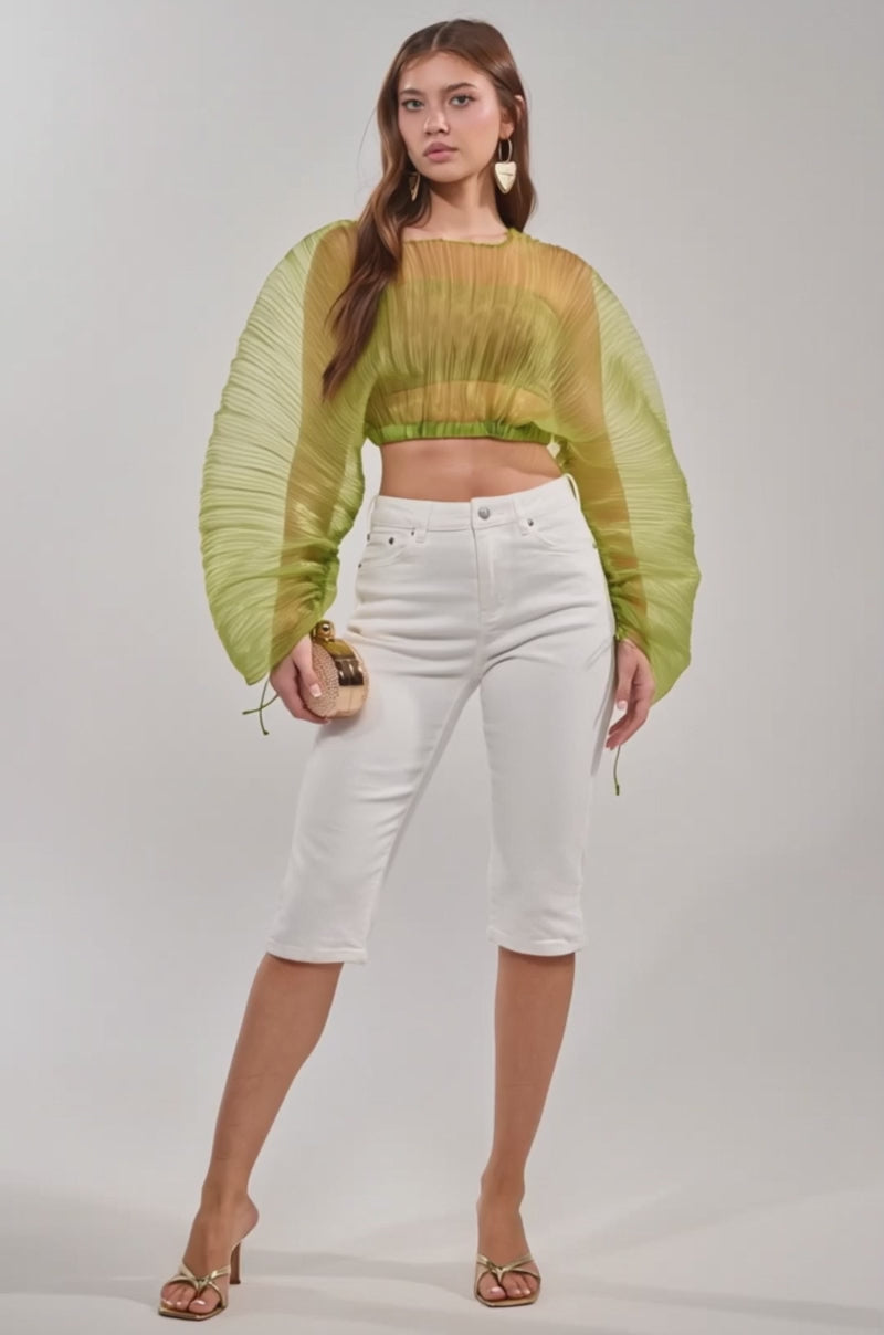 Video of woman modeling the BEYOND PRETTY PLEATED COCOON BLOUSE IN GREEN, paired with white high-waisted pants and a small round beige clutch. She has long brown hair, statement earrings, and a confident expression.