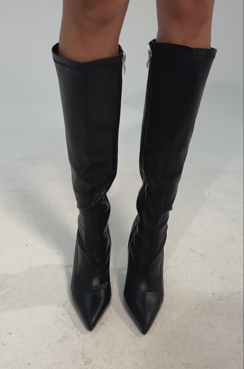 Video of woman modeling the AZALEA WANG CALANA BLACK 4 WAY STRETCH PU STILETTO BOOT, featuring sleek black faux leather, pointed toes, side zipper, and stiletto heels against a plain light background.