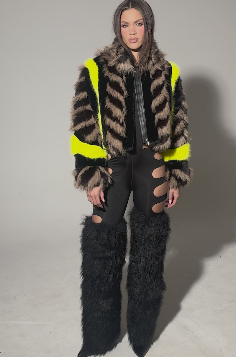 Video of woman modeling the MISS ME WITH THAT PANELED FAUX FUR jacket, featuring black, brown, and neon yellow stripes, over a black outfit with nude side cutouts against a neutral background.