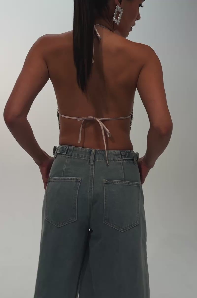 A video of a woman wearing the COOL GIRL LIKE ME BERMUDA SHORT, an embellished denim Bermuda short adorned with rose and religious-themed patches, gold-tone studs, and gold chains. 