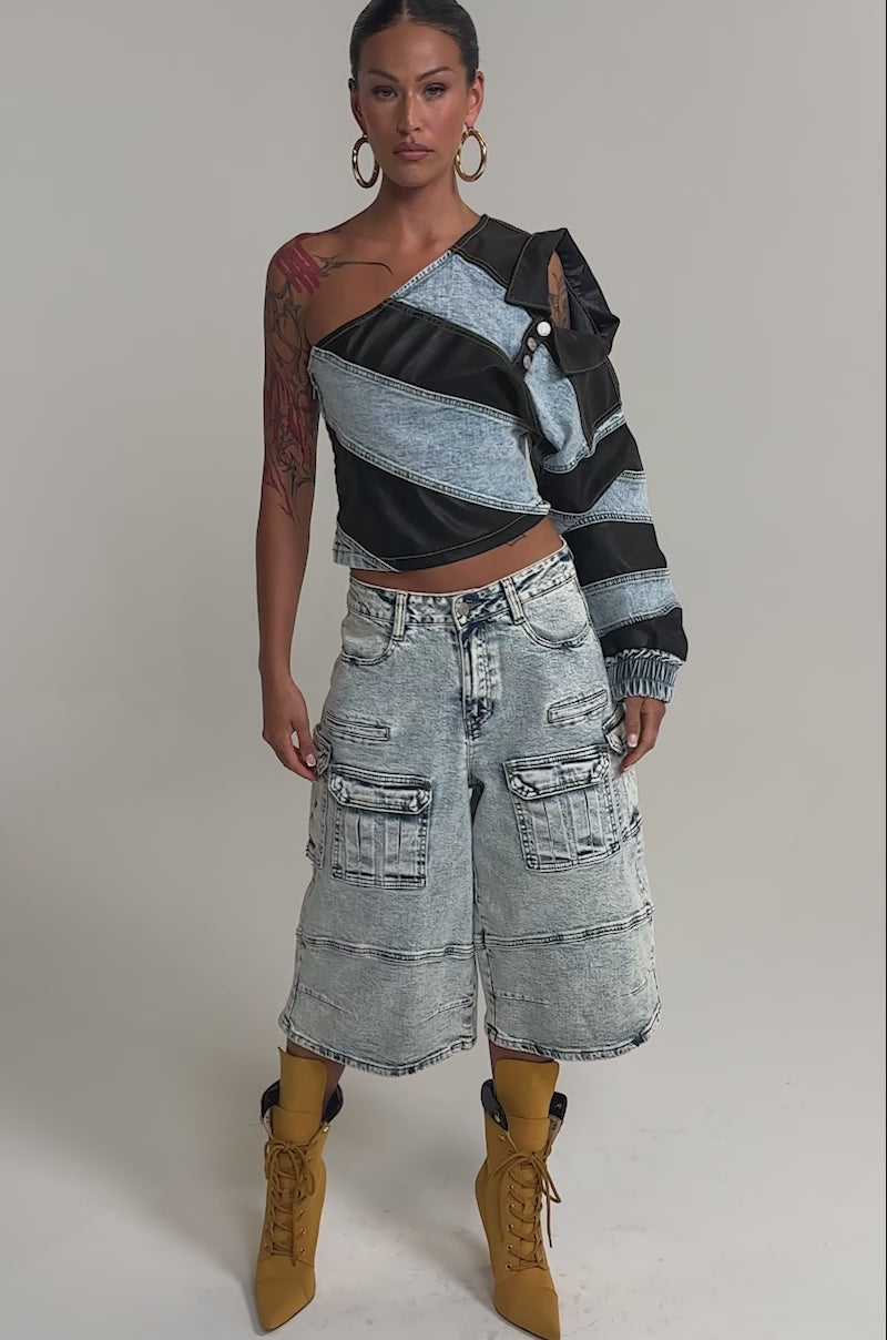 Video of woman modeling the DISILLUSIONED DENIM PU TOP—a unique off-shoulder denim top with black leather patches—paired with light wash cargo jeans, standing against a plain background.