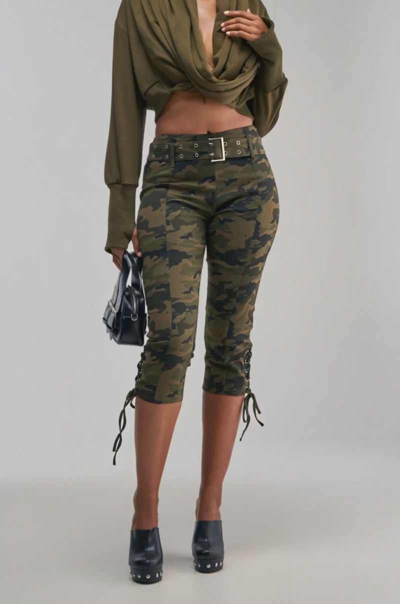 Video of a woman modeling the “JUST TOO COOL FOR YOU SWEATSHIRT IN OLIVE,” styled as a streetwear-inspired wrap, paired with camouflage cropped pants and black platform heels.