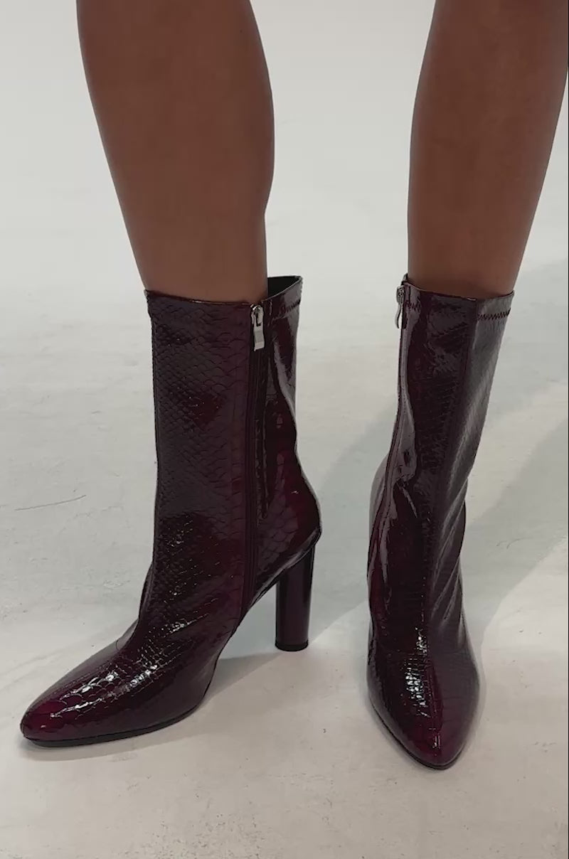 Video of woman modeling the AZALEA WANG WINGROVE BURGUNDY CHUNKY HEEL CROCODILE BOOTIE, featuring a shiny burgundy crocodile-embossed finish, pointed toes, and chunky cylindrical heels