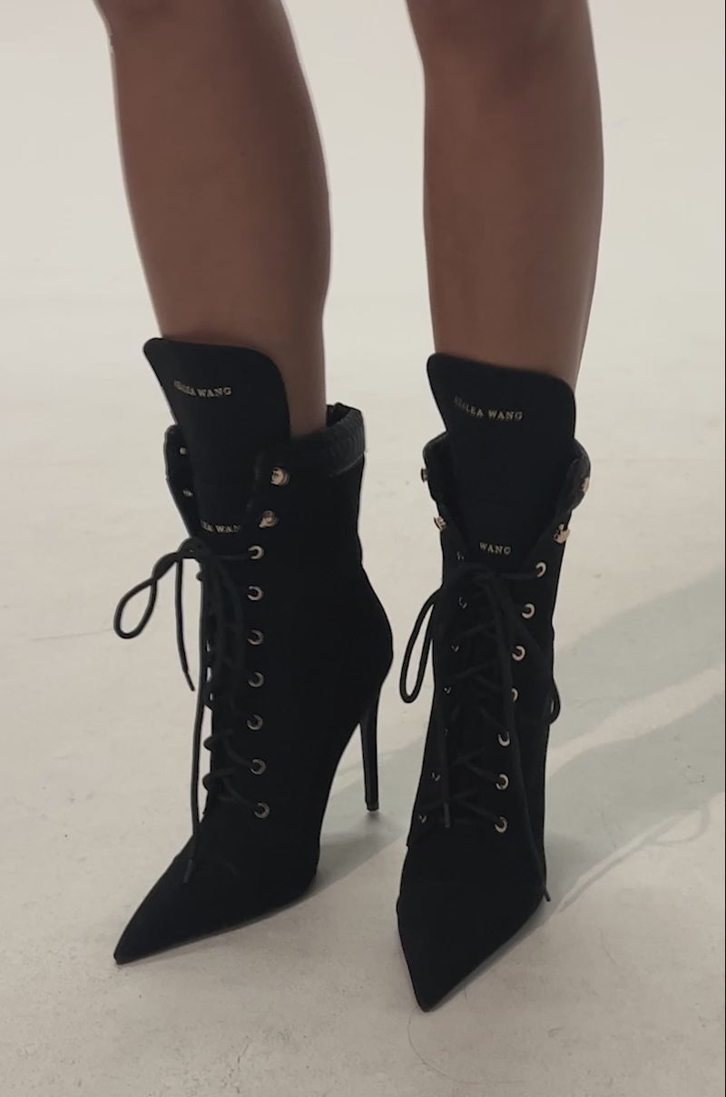 Video of woman modeling the AZALEA WANG XIOMARAN BLACK STILETTO BOOTIE featuring black suede, pointed toes, stiletto heels, gold eyelets, and "AZALEA WANG" on each tongue.