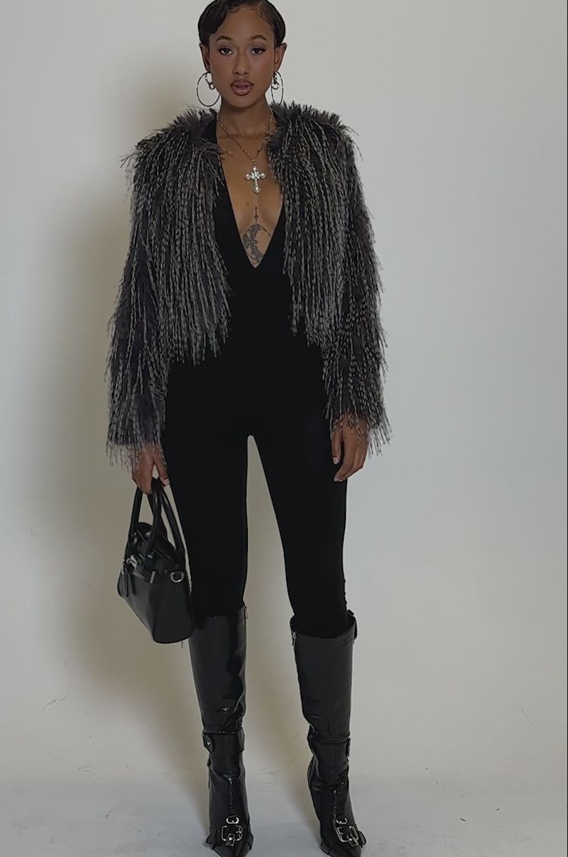 Video of woman modeling the BIRDS OF A FEATHER SHAGGY FAUX FUR jacket in dark gray and black, paired with fitted black pants and hoop earrings, standing against a plain light background 