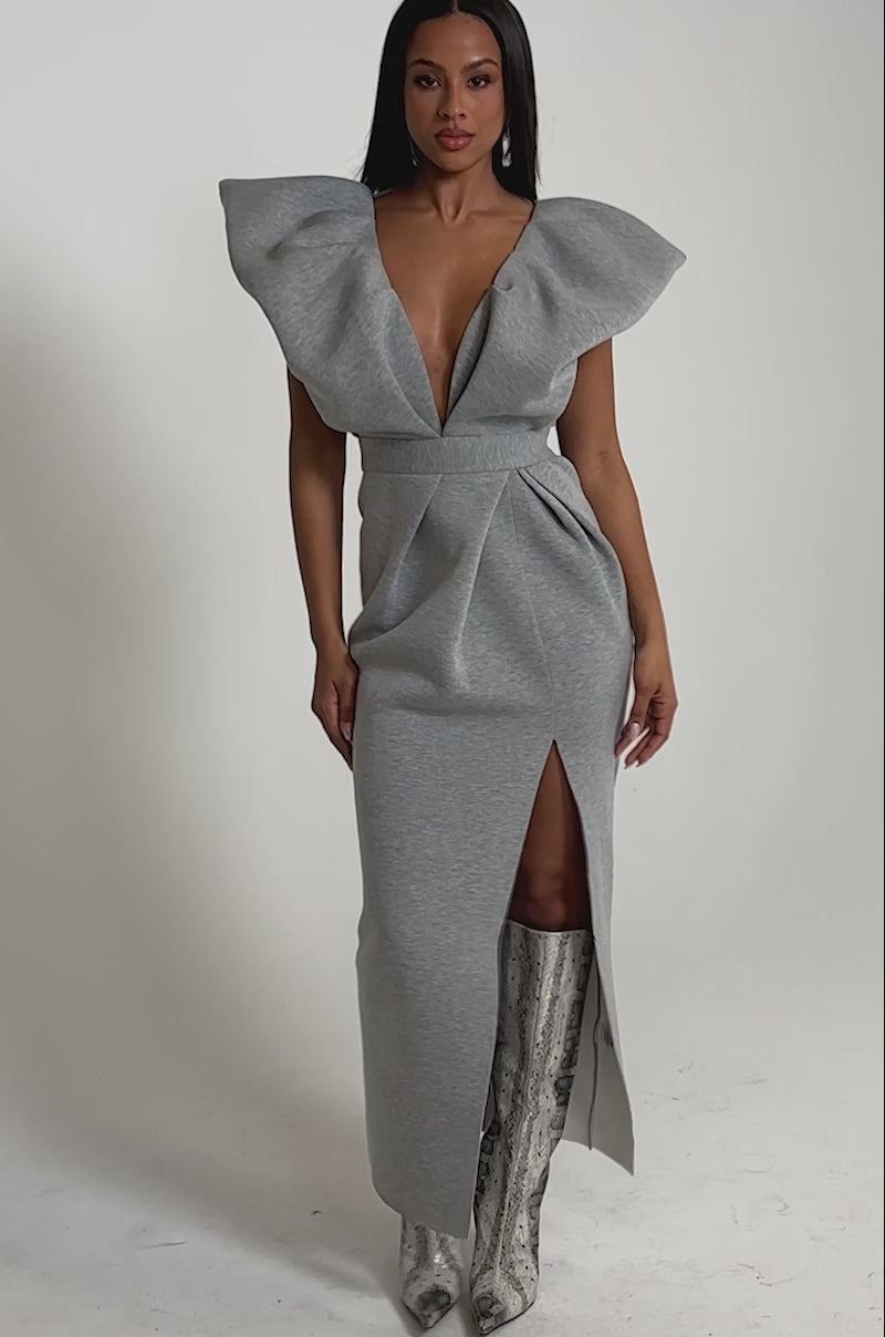 A video of a model wearing the MAKE YOU MINE MAXI DRESS featuring a deep V-neck and a thigh-high slit with knee-high snakeskin boots.