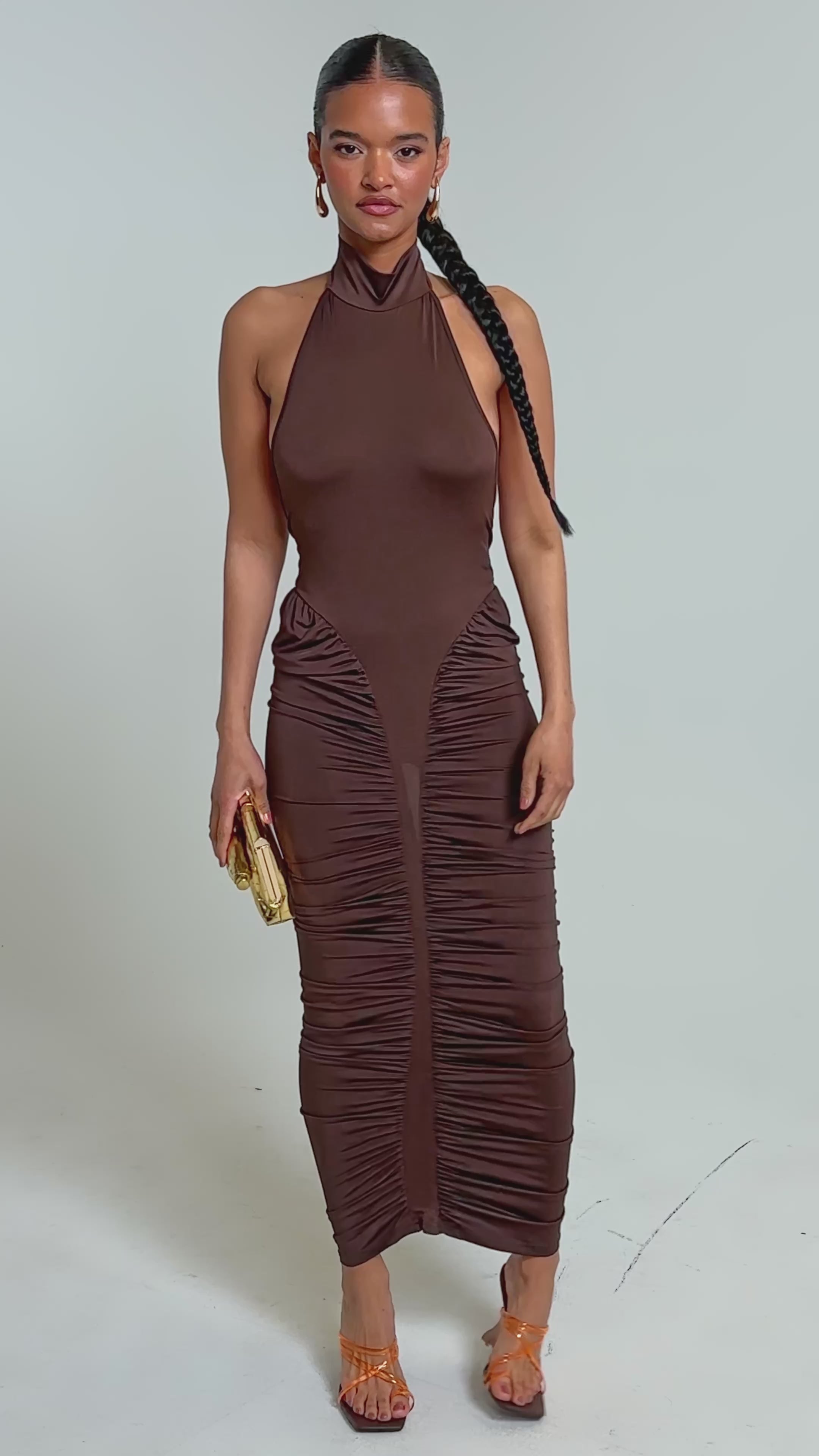 Video of woman modeling the HIPS DON'T LIE RUCHED MAXI DRESS, styled with orange strappy heels, a gold clutch, braided hair, and simple jewelry for an elegant look.