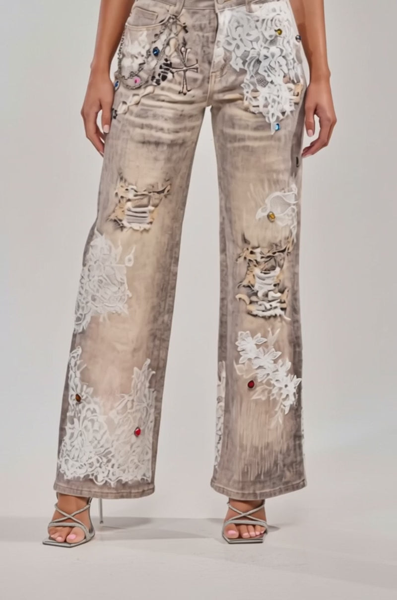 A video of a model wearing the DONT MESS WITH ME RELAXED DENIM—wide-legged jeans with lace details and colorful jeweled accents—styled with a white tank top and silver high-heeled sandals.
