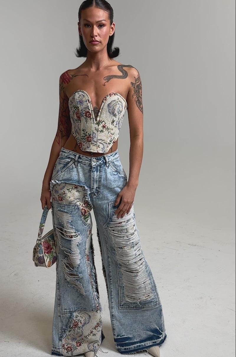 A video of a woman in the LANA DISTRESSED JEANS WITH JACQUARD DETAIL, paired with a strapless floral corset top and a matching small handbag. 