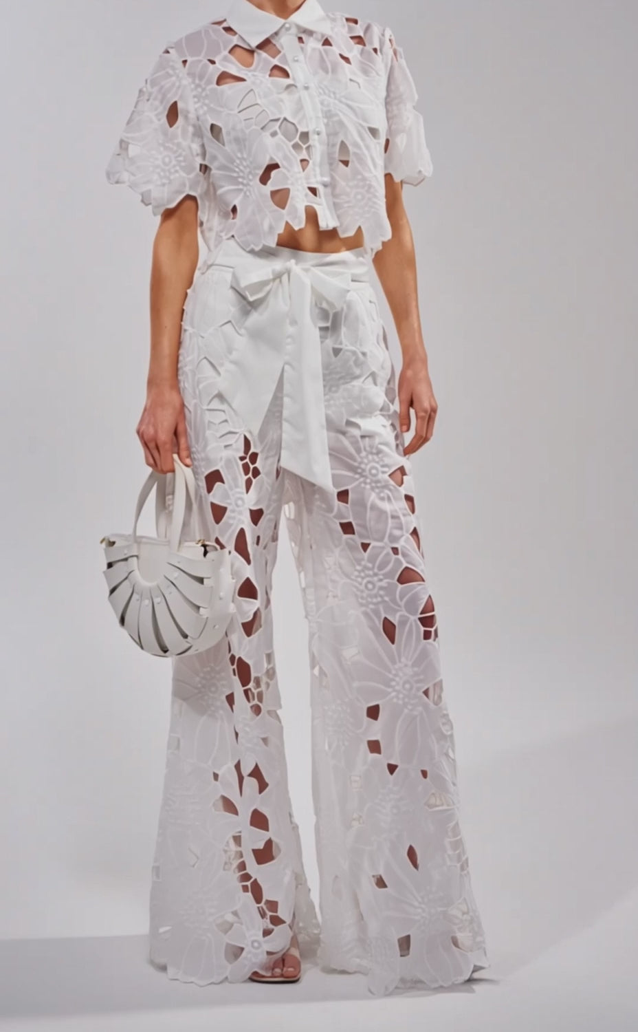 A video of a woman wearing the DOLLY FLORAL BUTTON DOWN IN WHITE, a matching cropped white floral lace shirt with wide-leg cut-out pants. 