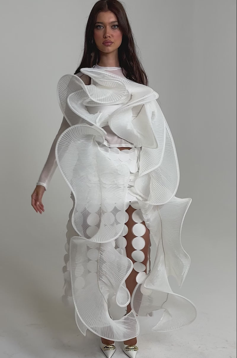Video of woman modeling the DRAMA RUFFLE BLOUSE, a white avant-garde top with dramatic ruffles and large circular cutouts, styled with gold pointed-toe heels against a plain light background.
