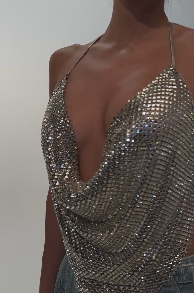 A video of a model wearing the DISCO CLUB COWL NECK TOP—a sparkly gold rhinestone crop top with a draped halter neckline—and high-waisted blue jeans.