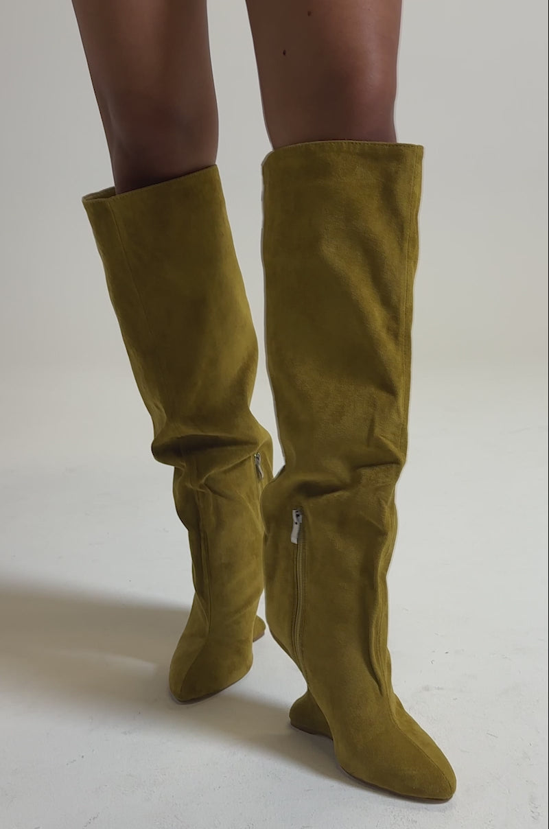 A video of a person modelling the AZALEA WANG VINCE MUSTARD FAUX SUEDE WEDGE BOOT—pointed toe, knee-high, with a side zipper and slightly slouched design—against a plain light gray background.