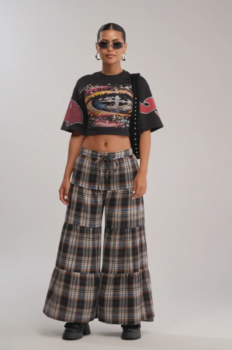 Video of woman modeling the EYES ON THE PRIZE GRAPHIC TEE featuring red and white sleeve designs, paired with high-waisted plaid pants
