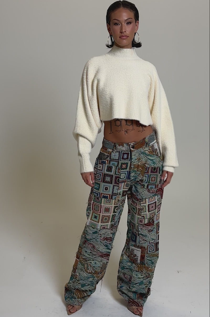 A video of a person in a cream, long-sleeve cropped sweater and WILD PATCHWORK TROUSER featuring a wide-leg silhouette. 