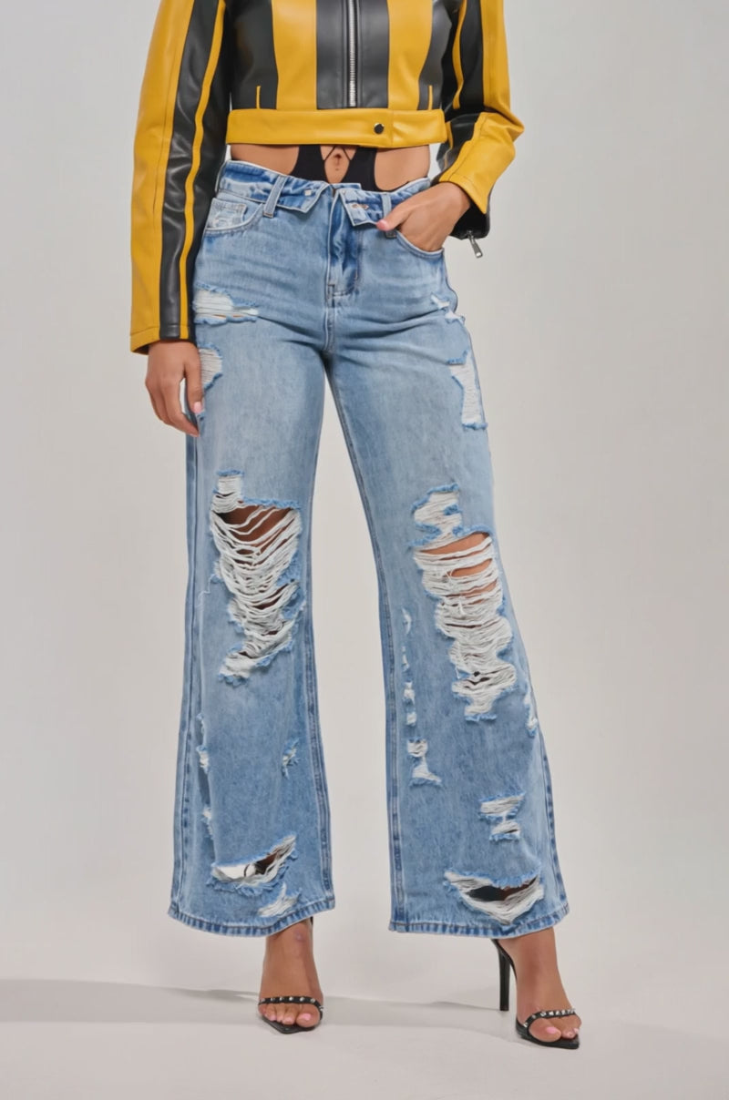 Video of woman modeling the SOMETHING NEW FOLD OVER WAISTBAND DISTRESSED DENIM jeans, styled with a yellow jacket featuring black stripes and black heeled sandals.