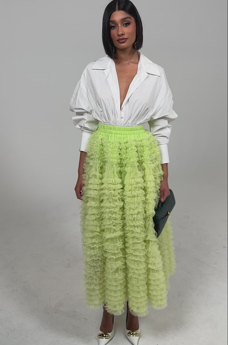 Video of woman modeling the LOVE THE DRAMA MESH MAXI SKIRT in light green, gold heels, statement jewelry, and a textured dark green clutch against a plain background.