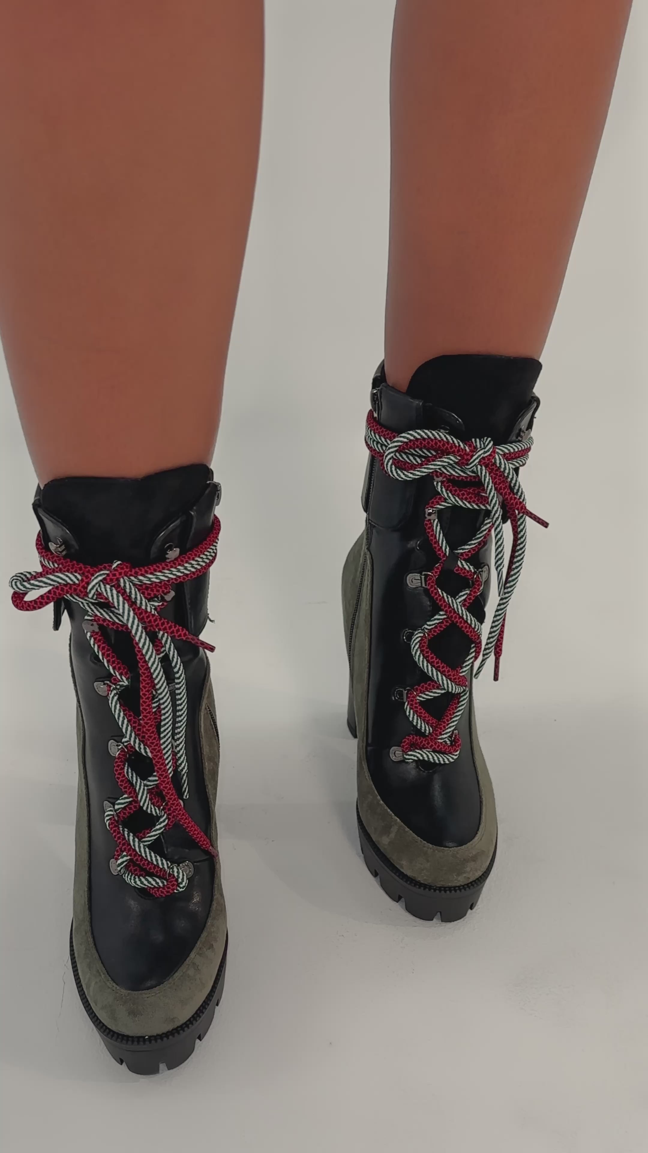 A video of a person wearing the AKIRA GOLD MUFFLER GREENMULTI CHUNKY HEEL BOOTIE which features green faux suede sides, black leather fronts, red-and-green striped laces tied in bows, a platform lug sole, and a chunky heel.