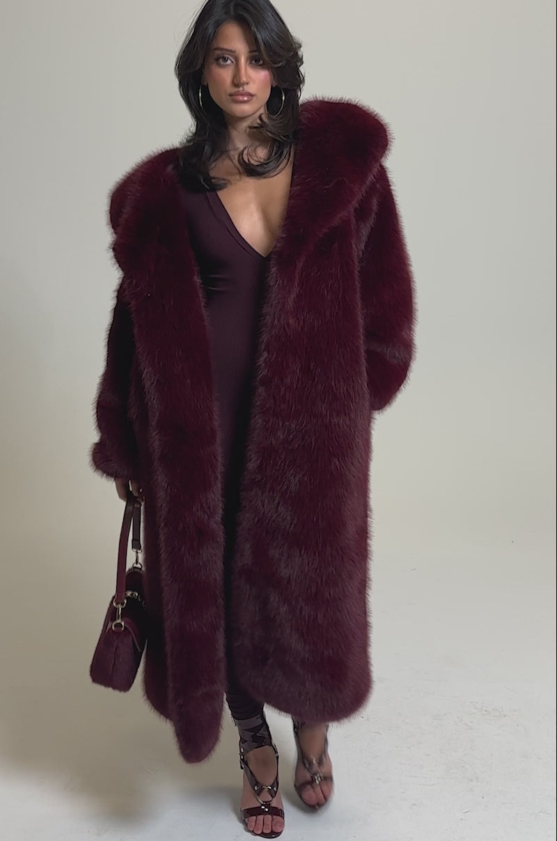 A video of a woman wearing the DEEP V LONG SLEEVE JUMPSUIT IN RAISIN with strappy high-heeled sandals against a plain gray background.