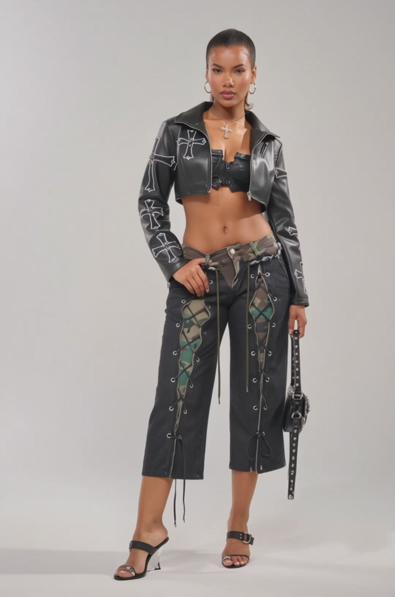 Video of woman modeling the WALK THAT WALK CAPRI PANT, paired with a black cropped leather jacket with silver cross designs, a black bustier top, black heels, and a matching studded handbag.
