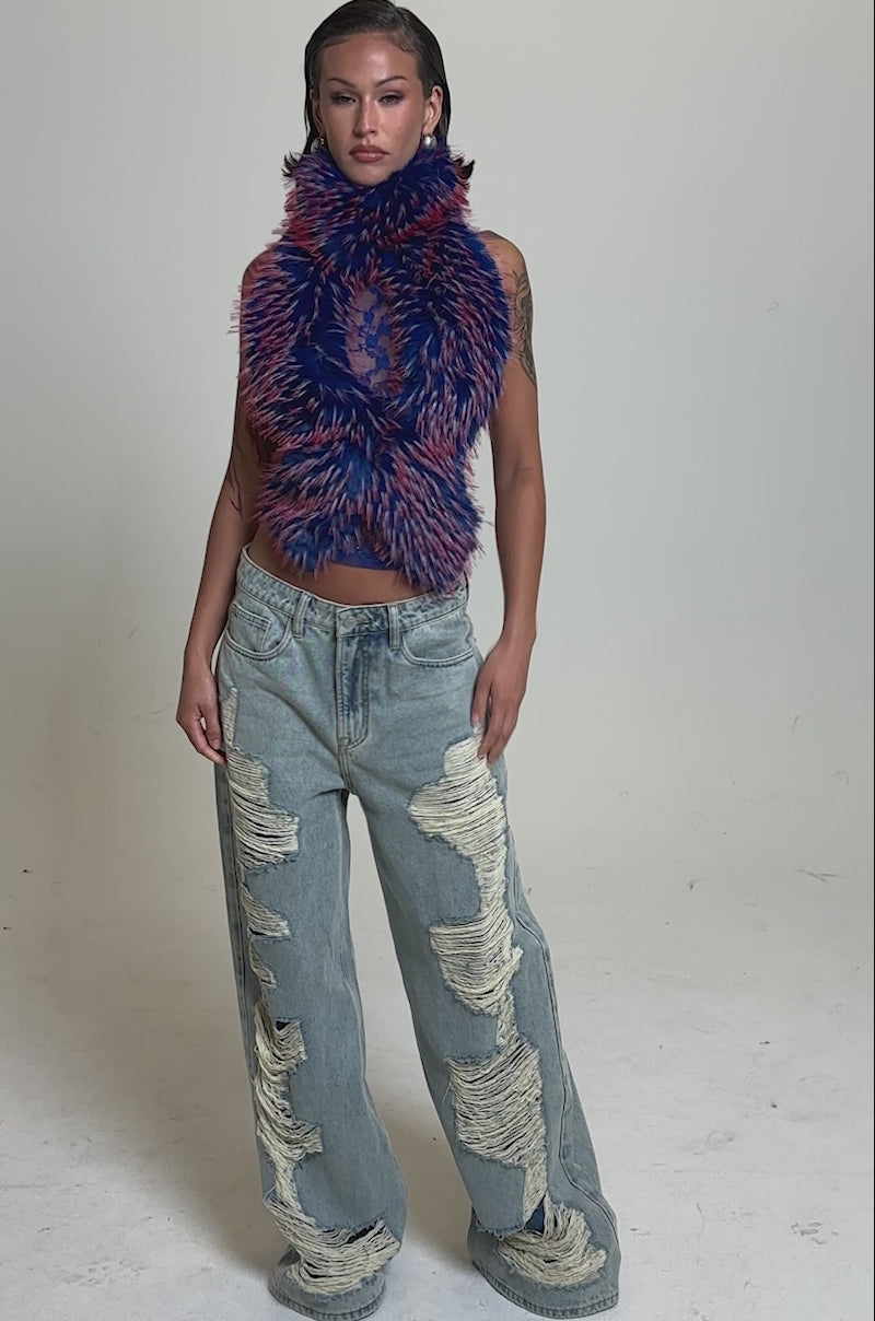 A video of a woman in the FEEL ME BABY FUR BLOUSE IN BLUE—a sleeveless, textured faux fur crop top—paired with light blue, wide-leg ripped jeans, posing with one hand in her pocket against a plain background.