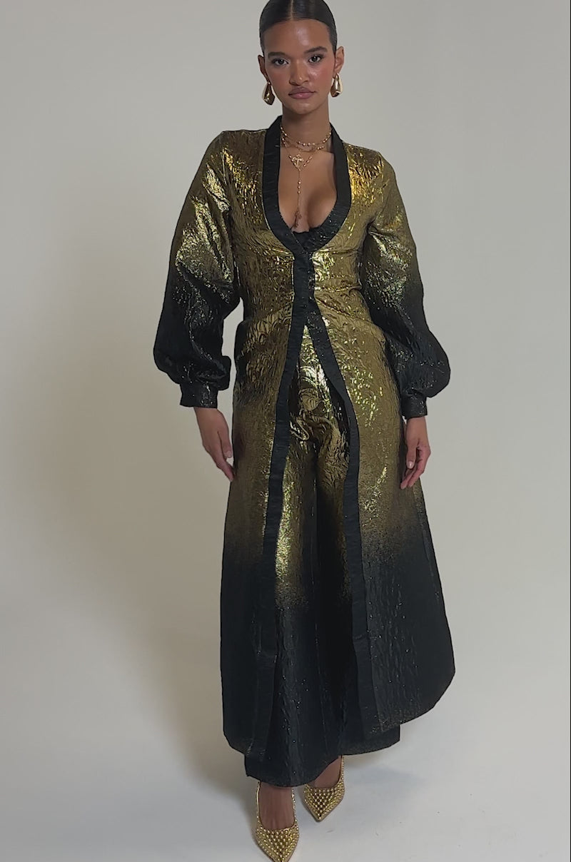 Video of woman modeling the ALL ABOUT THE DRAMA TROUSER—high rise, festive pants with a metallic gold-to-black ombre effect and textured fabric—paired with gold pointed-toe heels. 