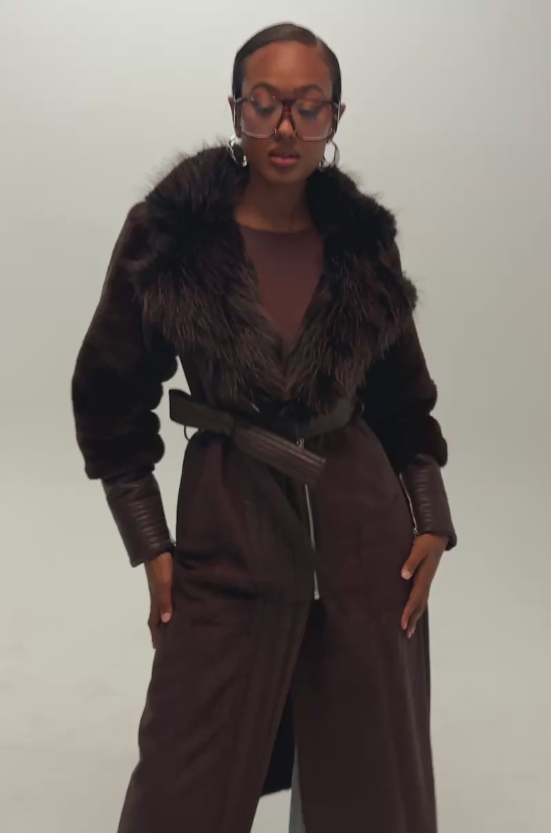 Video of a woman modeling the GOODIE MIXED MEDIA COAT IN BROWN with leather details, wide sleeves, and a belt.