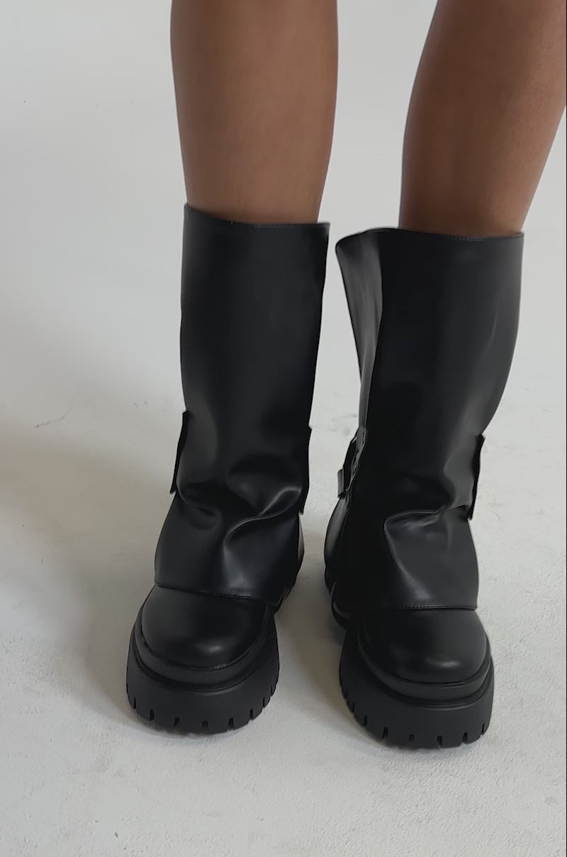A video of a person wearing the AZALEA WANG POWERLINE BLACK HARDWARE EMBELLISHED COMBAT BOOTIES with studded straps.