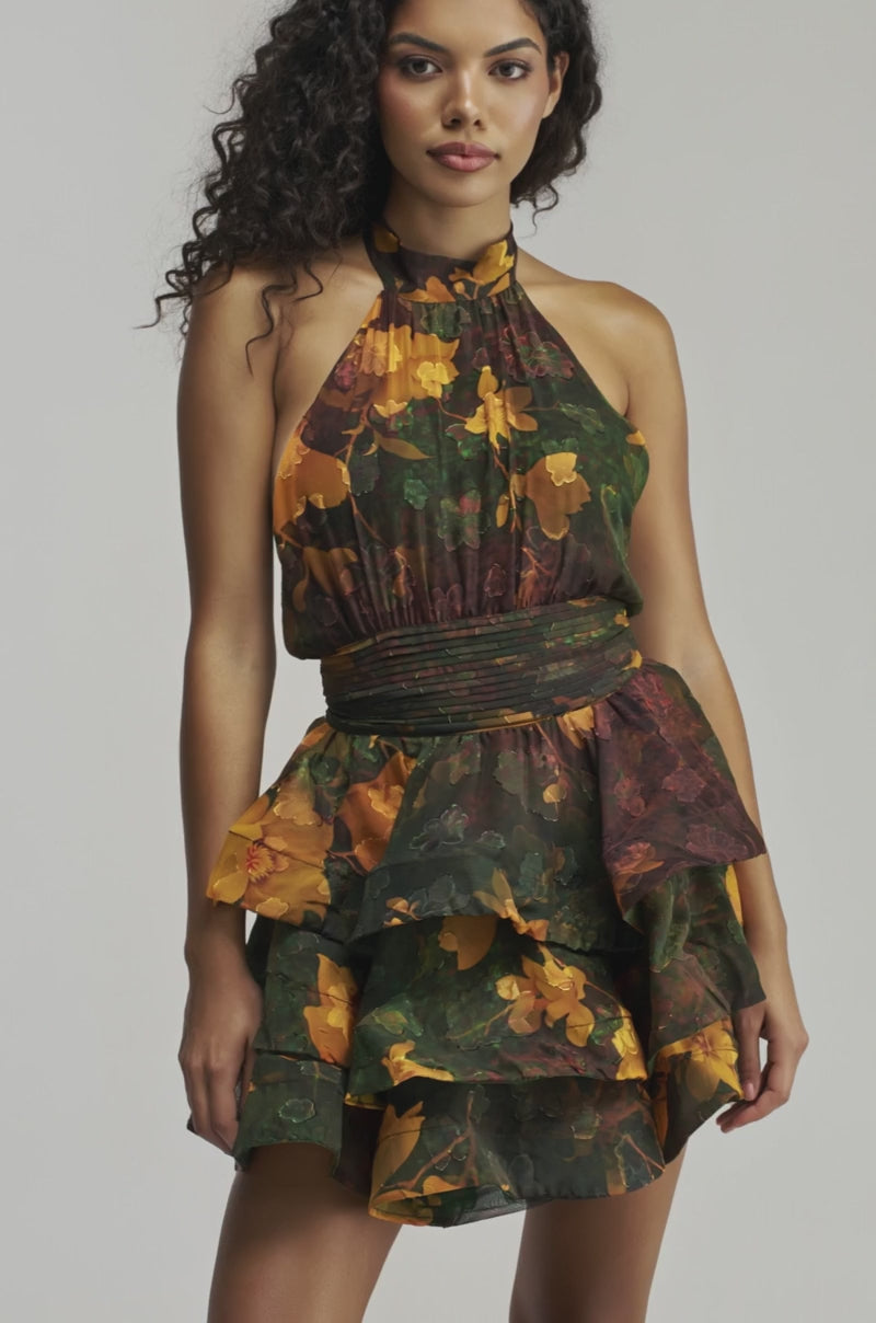 Video of woman modeling the SPIN ME AROUND CHIFFON MINI DRESS IN GREEN FLORALS — a sleeveless, ruffled mini dress featuring a dark green and yellow floral print. 