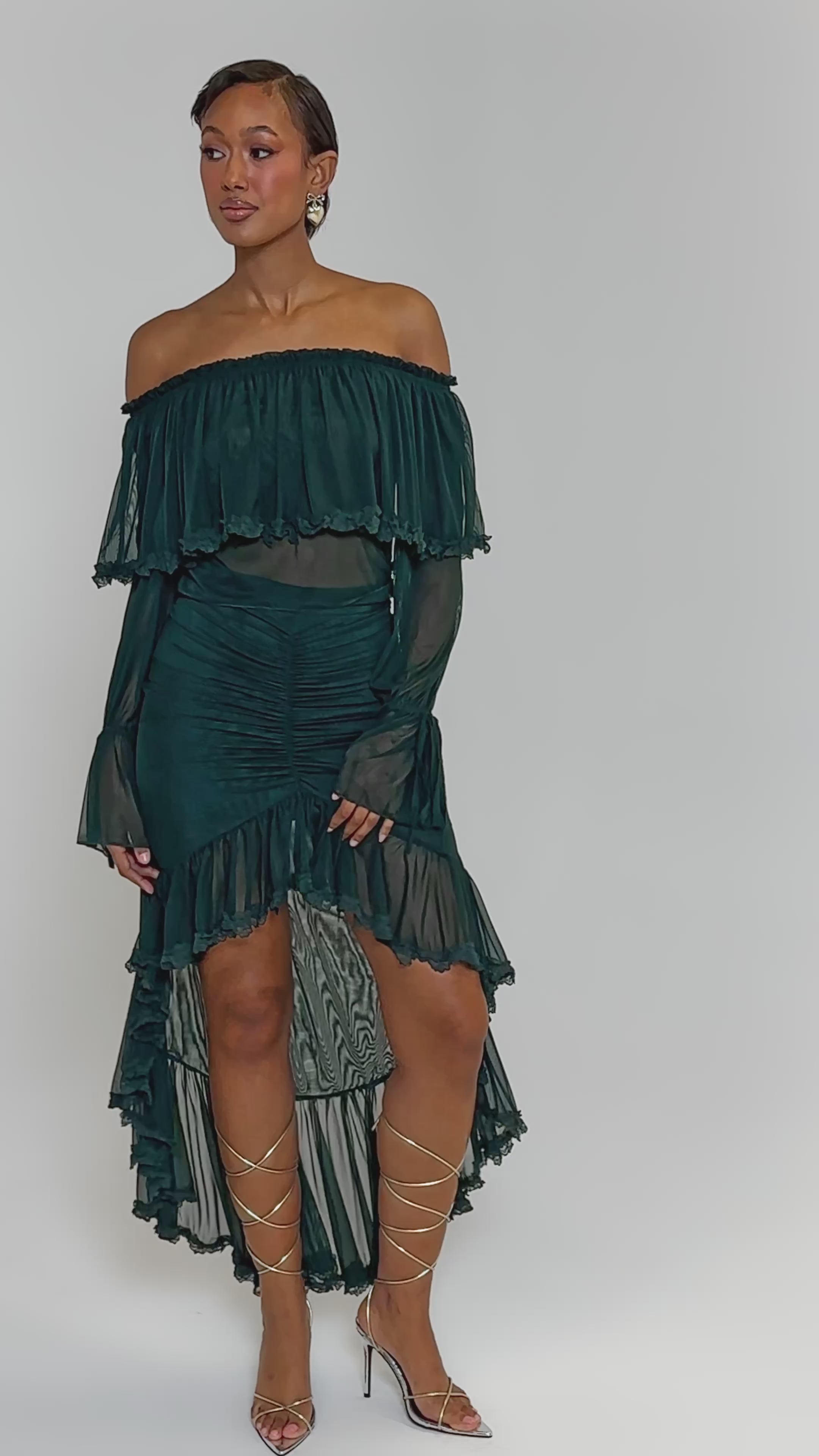 Video of woman modeling the EMERALD LOVER BLOUSE—an elegant, dark green, off-the-shoulder top featuring sheer ruffled layers and ruched detailing against a plain background.