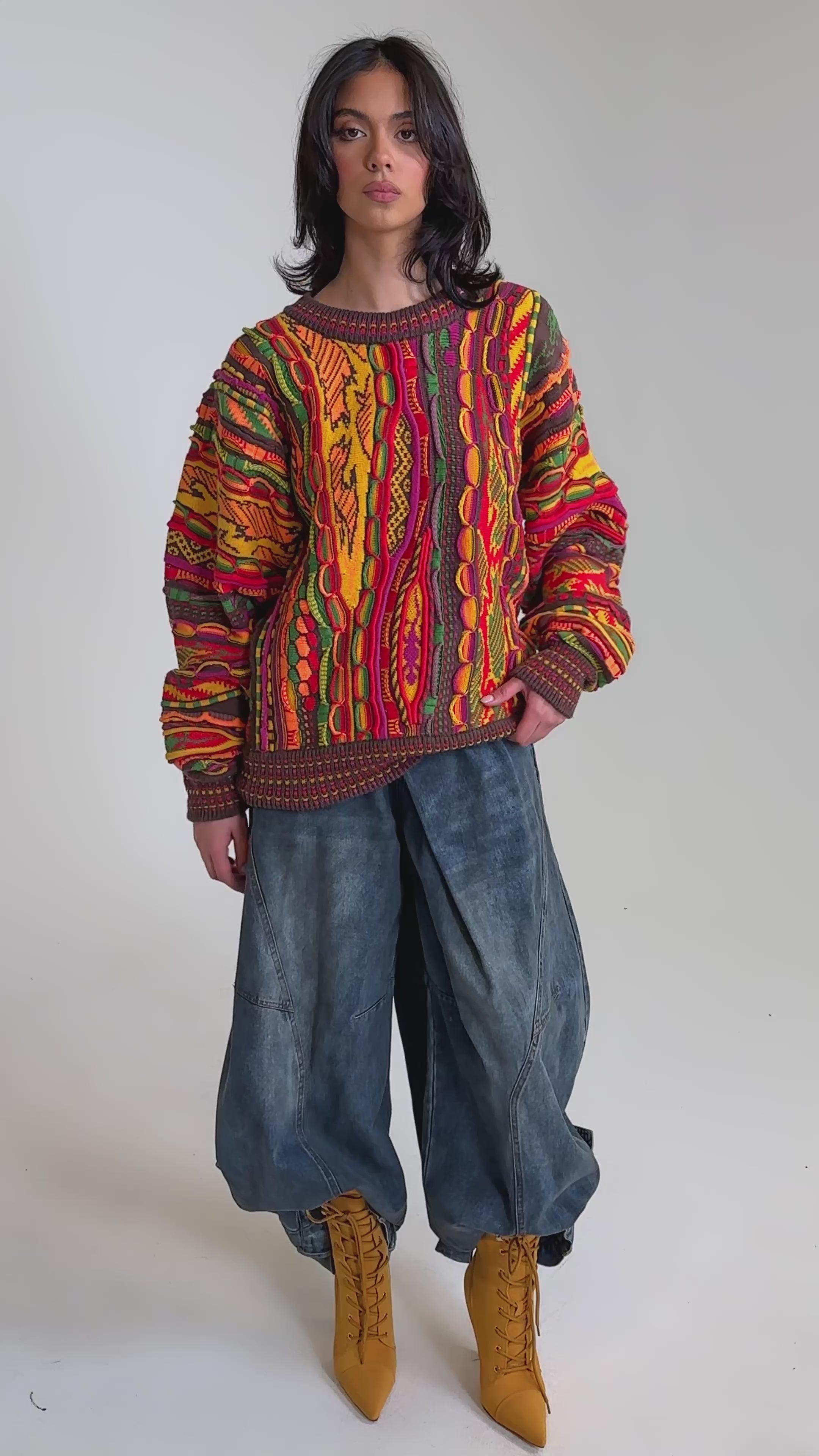 A video of a model wearing the THROWBACK SPECIAL KNIT SWEATER, oversized wide-leg jeans, yellow lace-up boots, and glasses.