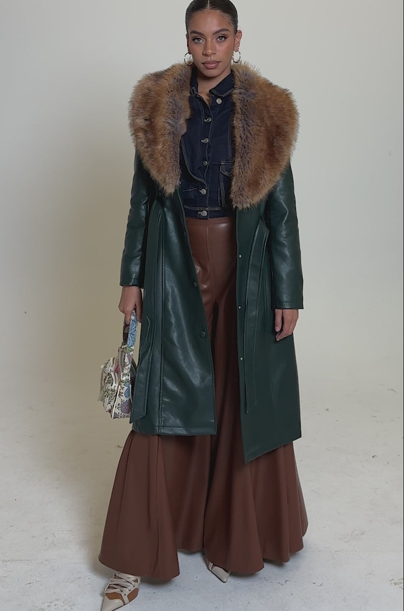 A video of a woman modelling wide-leg Galaxy Faux Leather Trousers in brown, a green leather coat with a large brown fur collar, a black cropped denim jacket, gold heels, and an embroidered handbag against a neutral background.