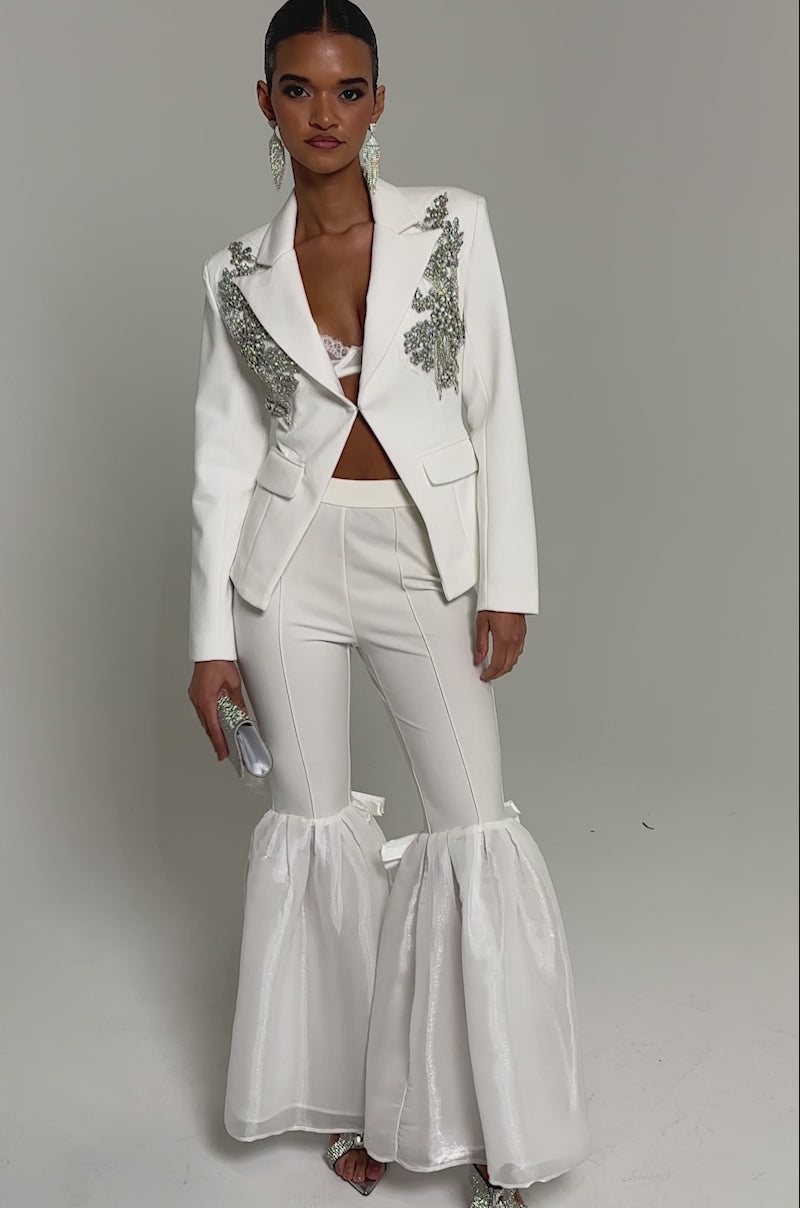 Video of woman modeling the SPEND IT ALL ON ME EMBELLISHED BLAZER—a white tailored blazer with silver details—paired with a metallic bralette, statement earrings, and a sparkling clutch.