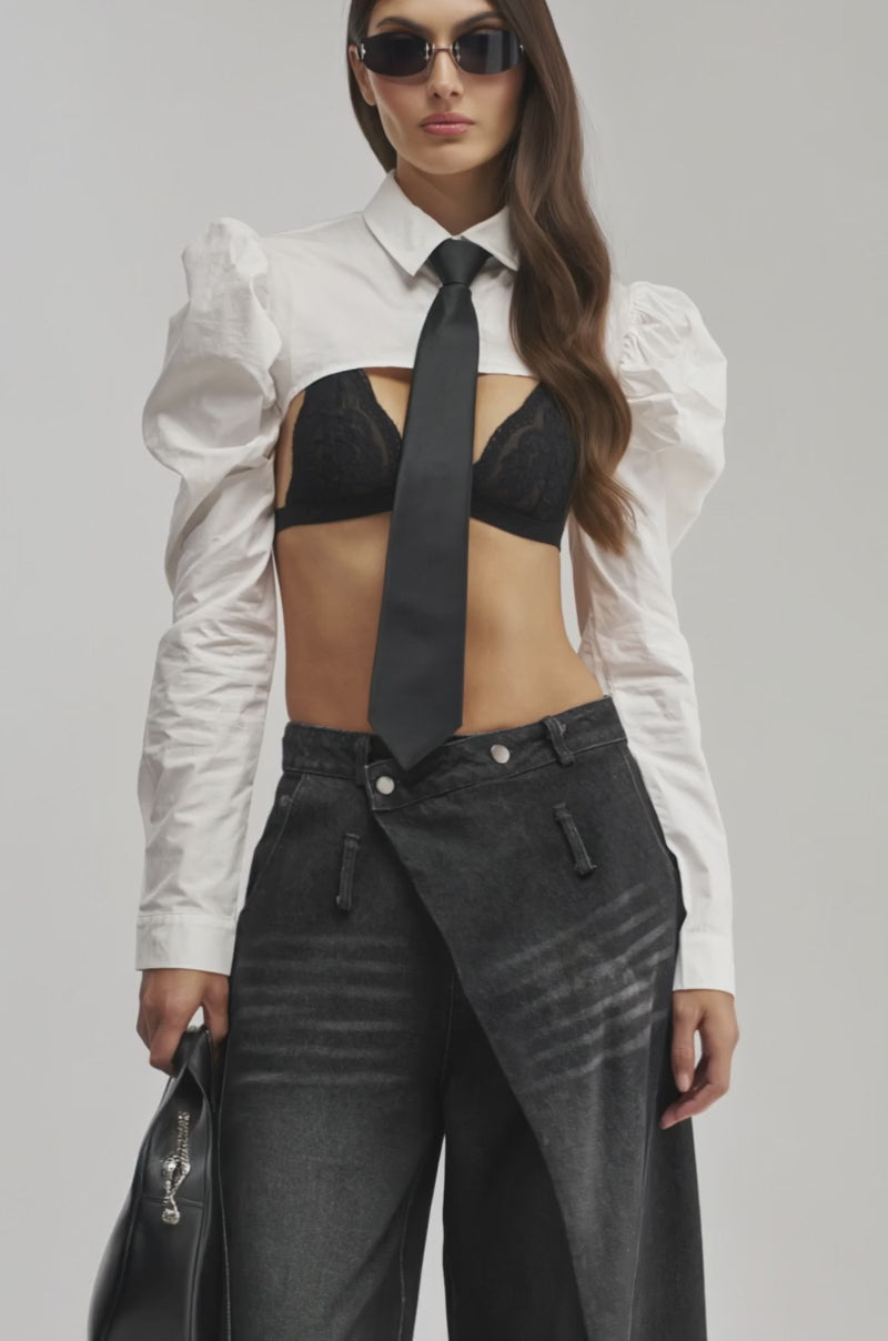 Video of a woman modeling the BACK TO BIZ POPLIN BOLERO TOP with puffy sleeves, styled over a black lace bra, and black tie.
