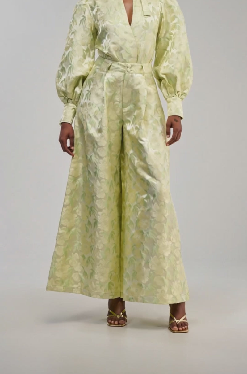 Video of a woman modeling the LOOK THIS WAY SHINY PANT IN GREEN—a pair of light green, wide-leg pants that showcase an elegant jacquard-inspired pattern.
