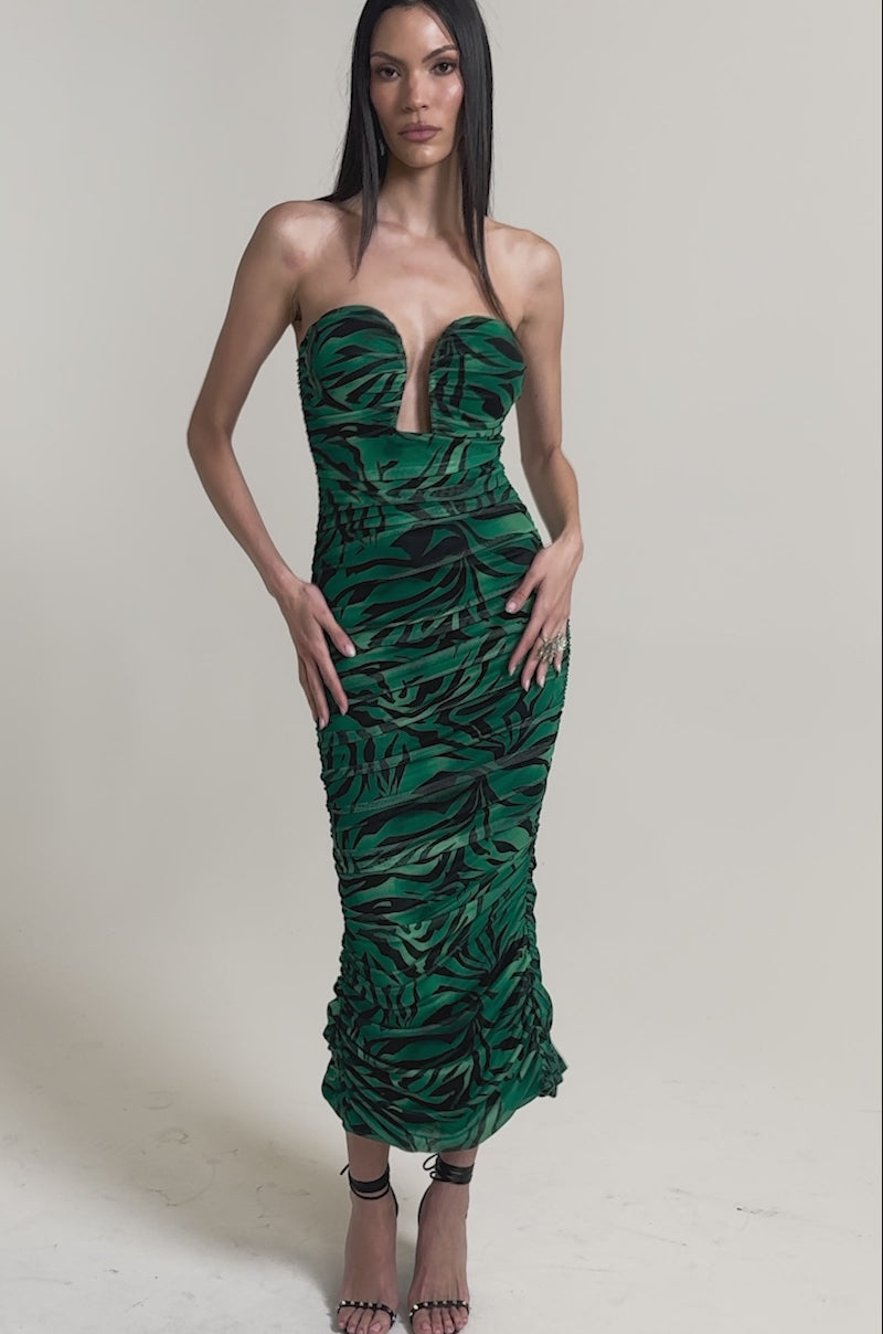 A video of a woman in the DAY OUT STRAPLESS PRINT MIDI DRESS—a strapless, form-fitting green zebra print midi dress with a bold black leaf pattern and deep V neckline—paired with high-heeled sandals against a plain light background.