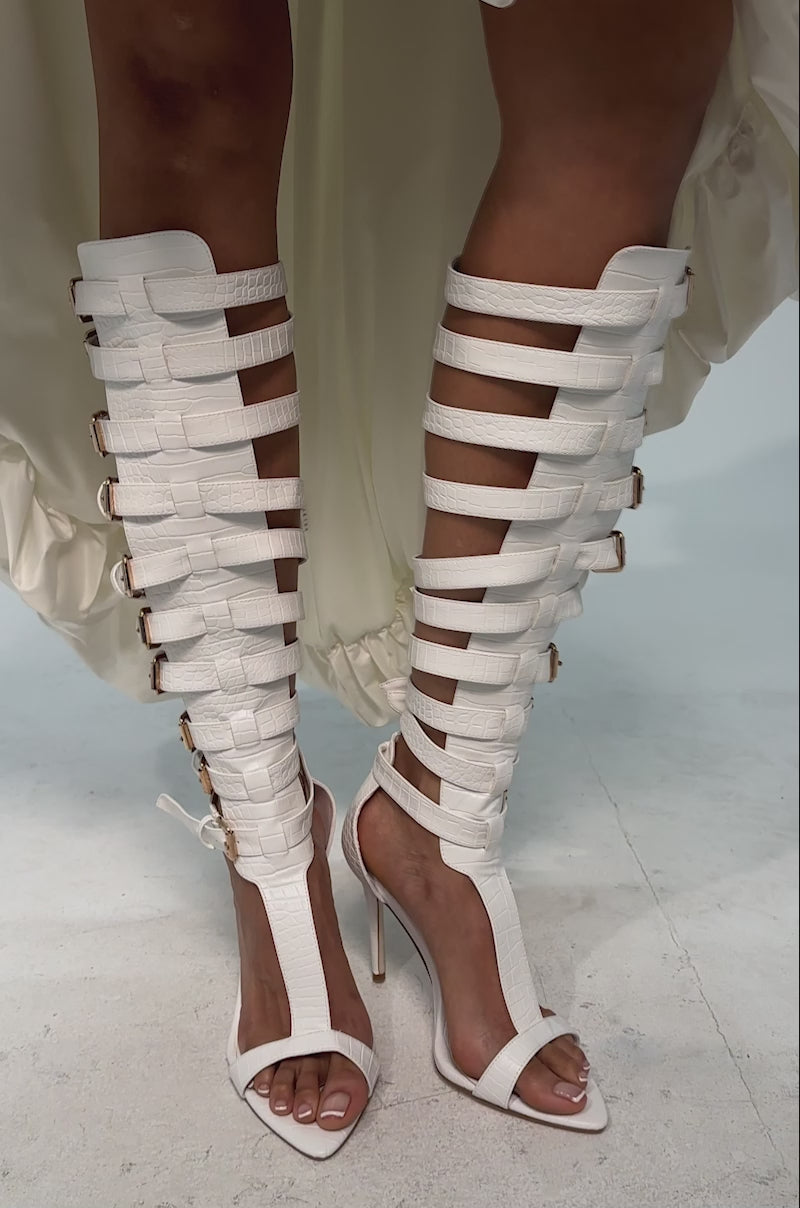 A video of a model wearing the AZALEA WANG CHERLLI WHITE CROC OVER THE KNEE SANDAL which features white croc-embossed faux leather, multiple ankle straps with gold buckles, an open toe, and a tall stiletto heel.