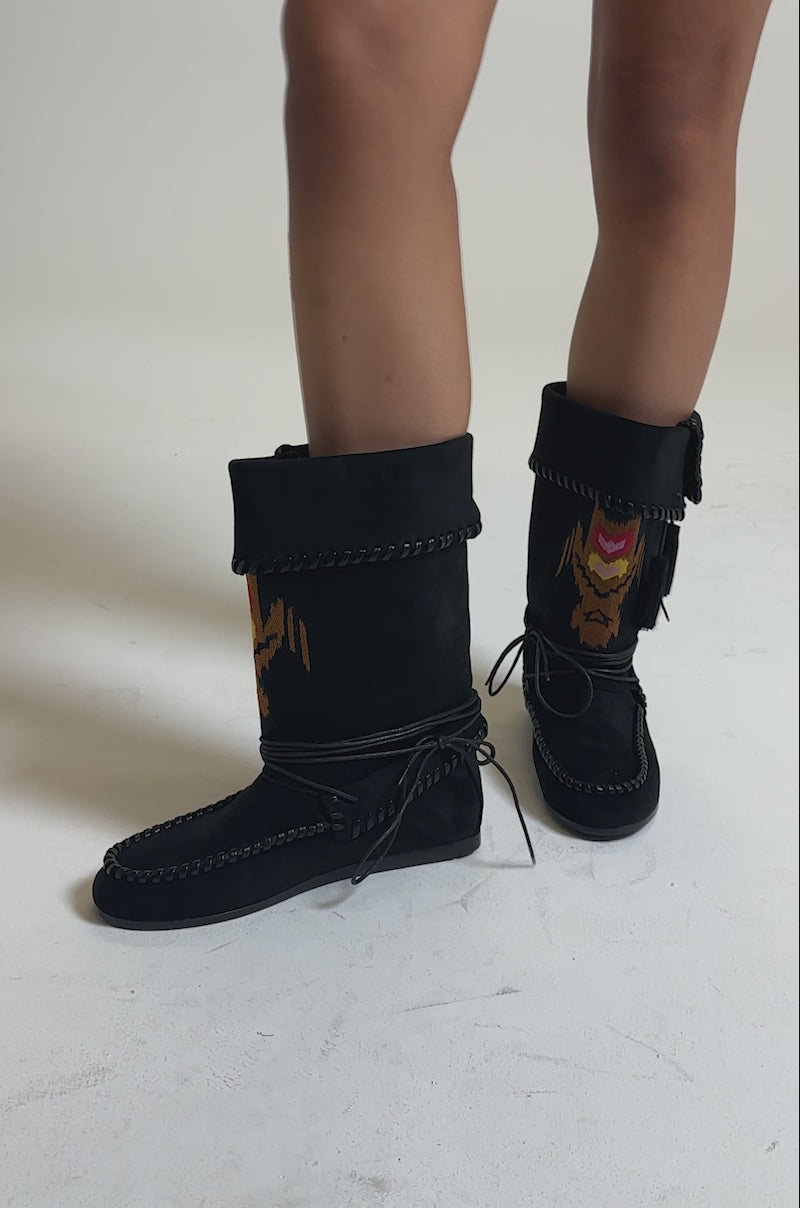 A video of someone wearing the AZALEA WANG WERET BLACK FLAT BOOTIE, featuring decorative stitching, tassels, and colorful embroidered designs on the front.