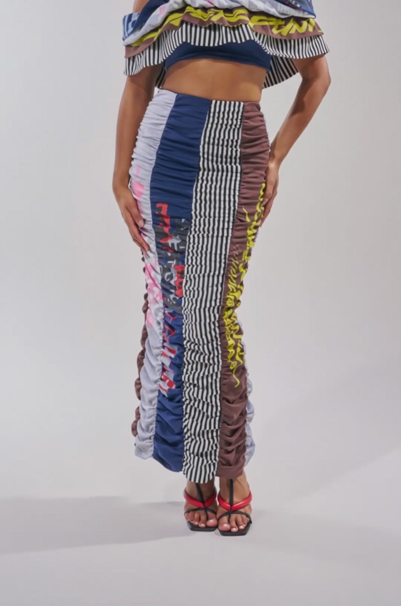 A video of a woman in the THAT GIRL GRAPHIC TEE TOP, styled strapless with ruffles from an upcycled tee, paired with a bold high-waisted ruched maxi skirt. 