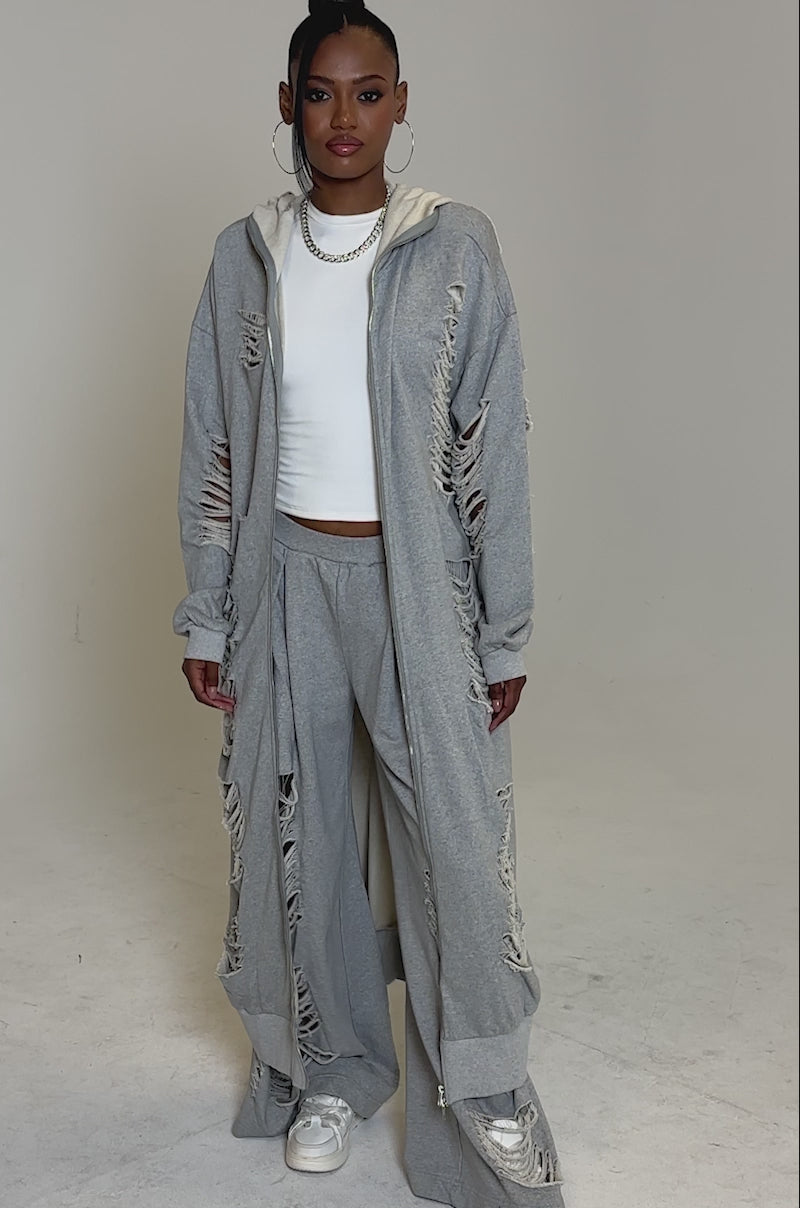 Video of woman modeling the STRESS HIM OUT LONGLINE SWEATSHIRT and matching distressed wide-leg pants with ripped details, accessorized with hoop earrings and white sneakers, against a plain white background.