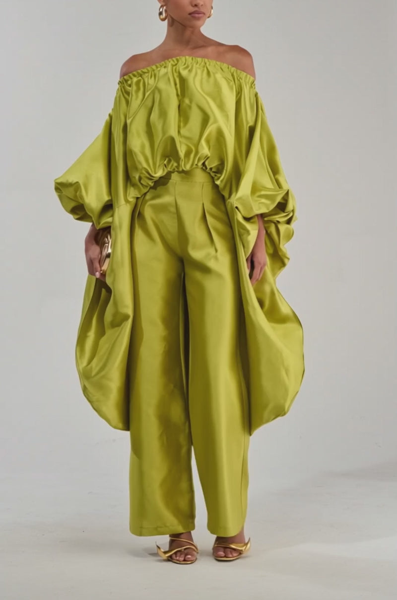 Video of a woman modeling the BY MY SIDE HIGH LOW BLOUSE IN CHARTREUSE, styled off-the-shoulder with voluminous sleeves and paired with wide-legged pants.