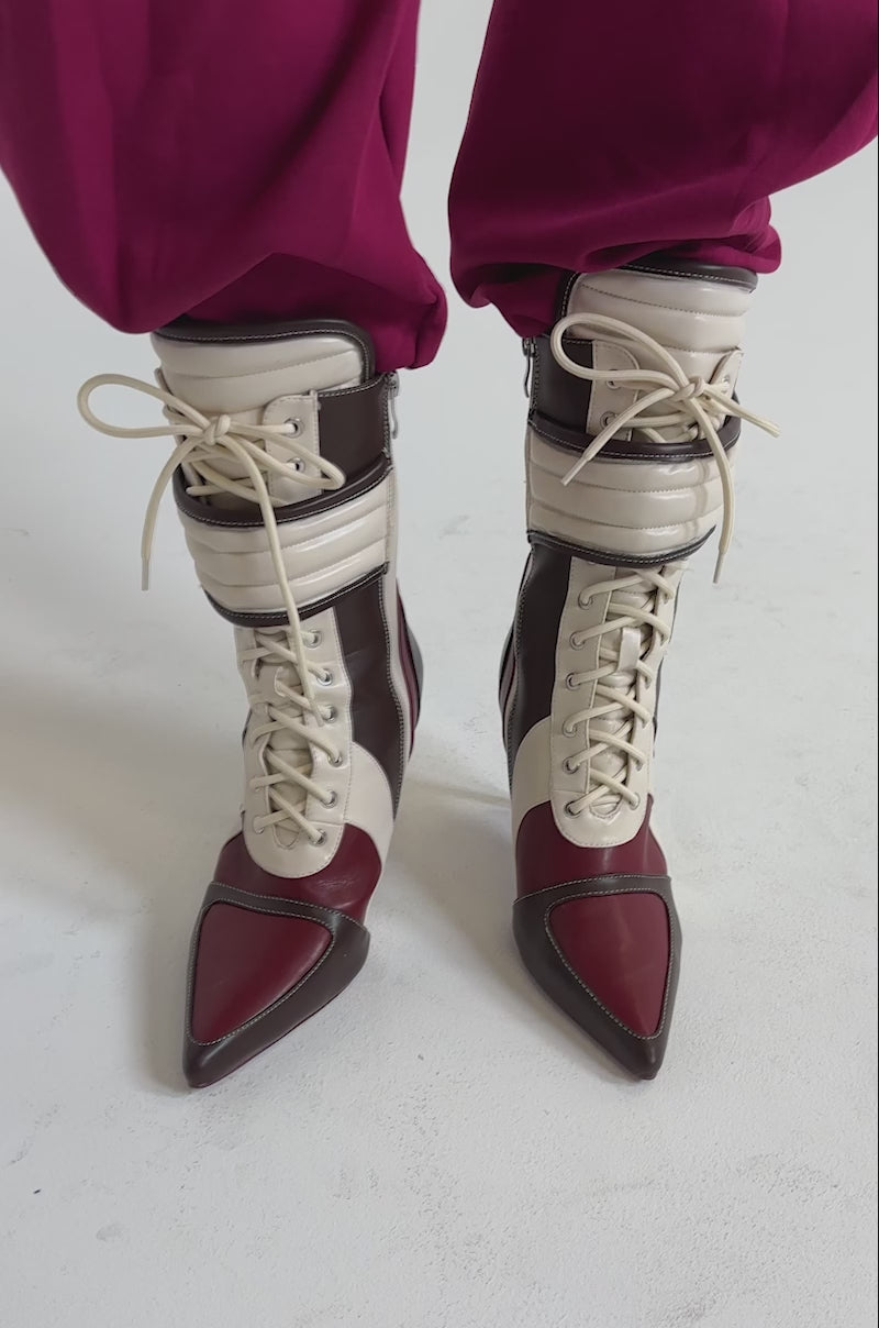 A video of a person wearing loose, bright pink pants tucked into AZALEA WANG AMADA BROWN SPORTY STILETO BOOTIES, which have pointed toes and a patchwork design in cream, burgundy, and brown leather.