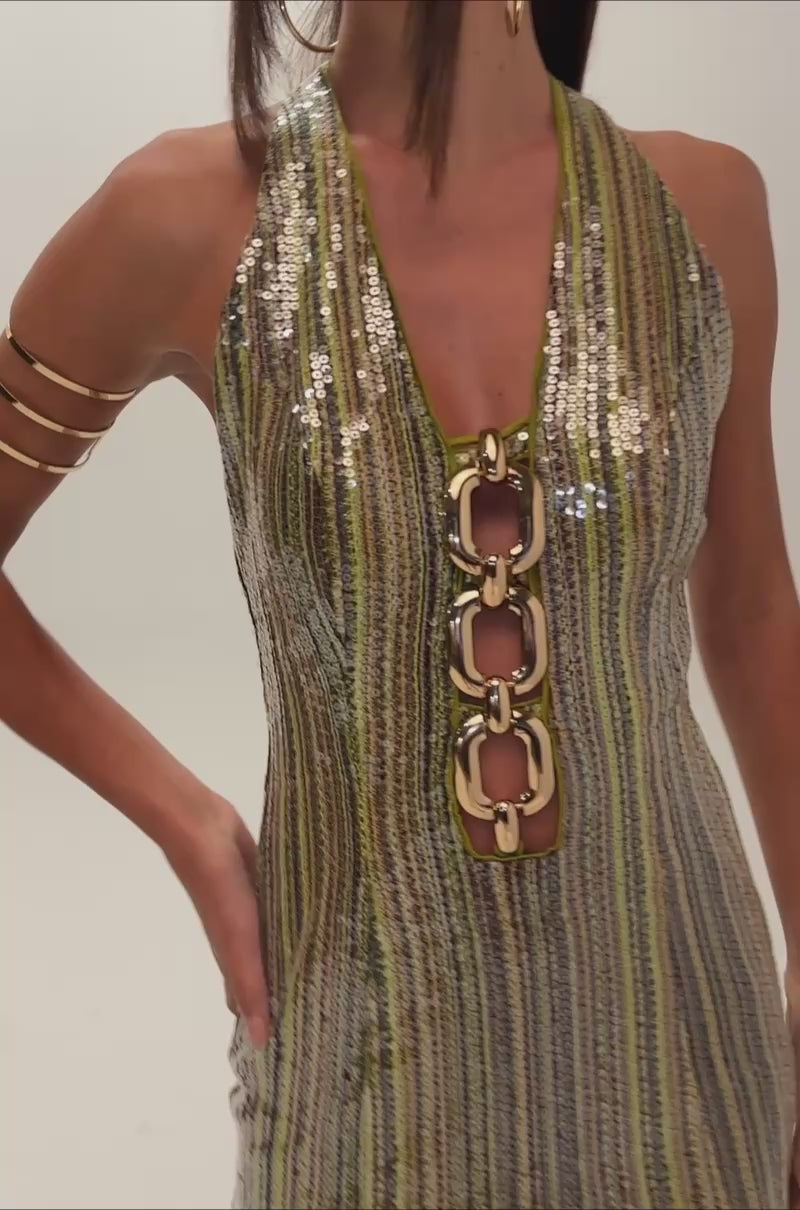 A video of a woman wearing the SPOTLIGHT SEQUIN MINI DRESS featuring vertical gold and silver sequin stripes and a bold chain neckline. 